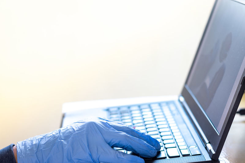 A man in blue gloves work on his laptop from home, corona virus