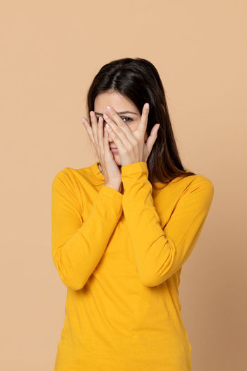 Portrait of young woman covering face against gray background