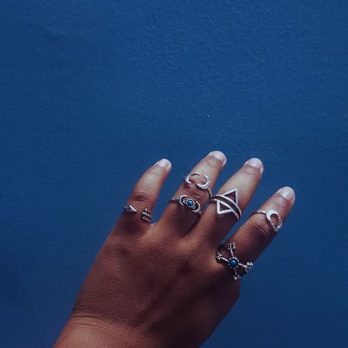 Cropped image of hand wearing rings against blue wall