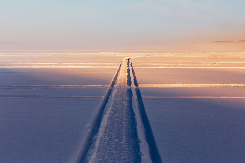Tire track on snow covered field against sky