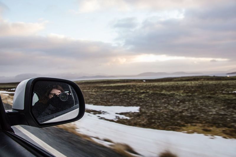 Reflection of woman photographing through camera in side-view mirror of car