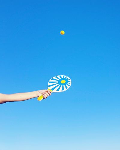 Low angle view of young woman playing ball against clear blue sky