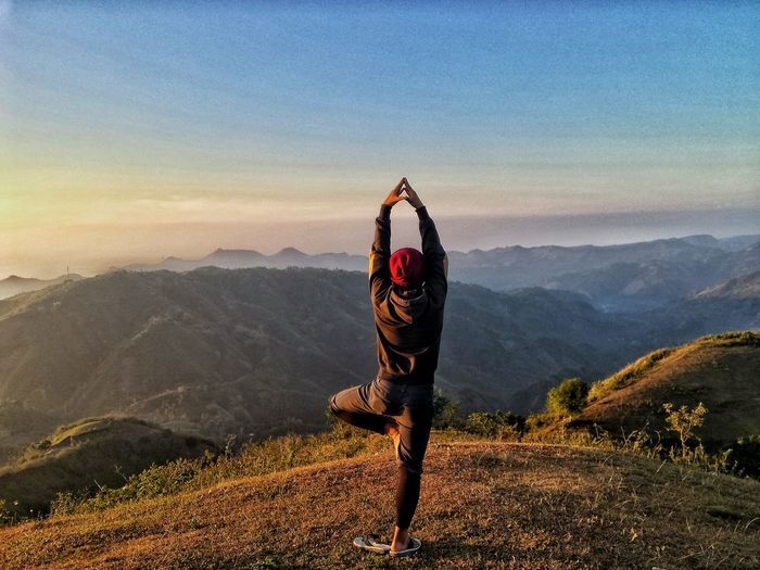 Rear view of man doing yoga pose on mountain