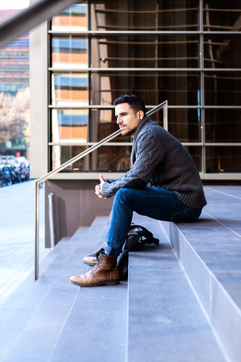 Young casual wearing man sitting at the entrance of an office building