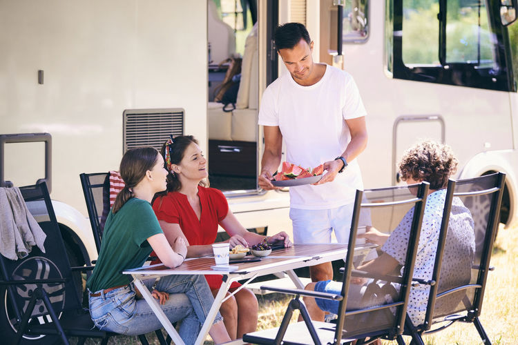 Man serving watermelon slices to family while camping at trailer park