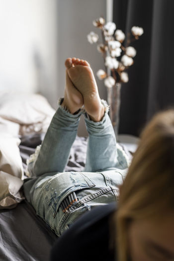 A woman lies on the bed with pencils in her jeans pocket.