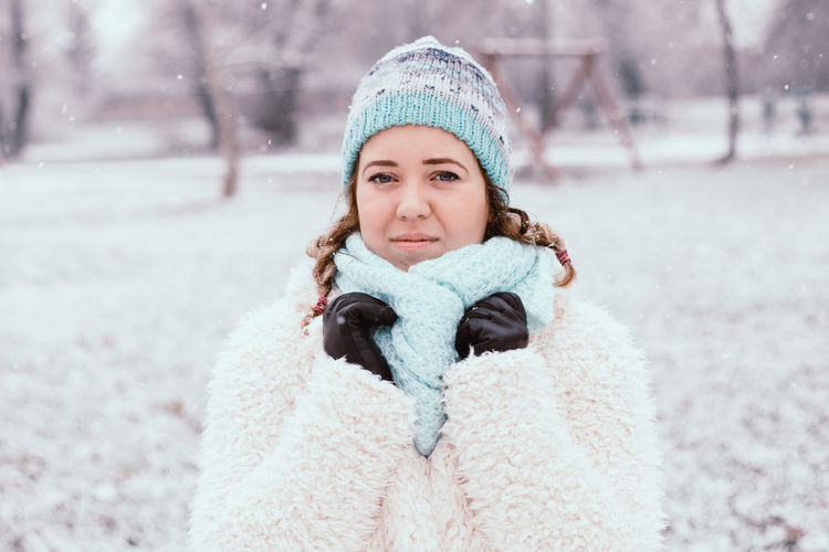 Portrait of smiling young woman in warm clothing standing at park during winter