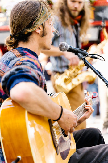 Selective focus on a young man singing and playing a guitar in the street