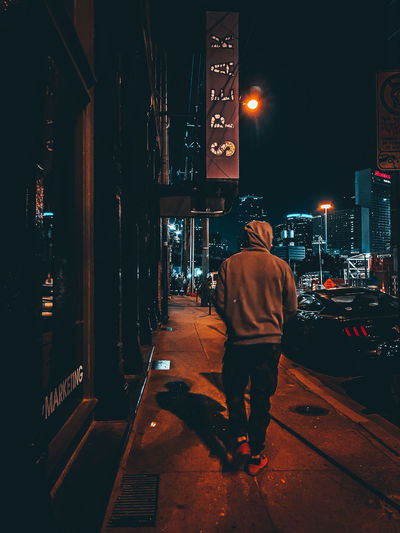 Rear view of man walking on sidewalk at night