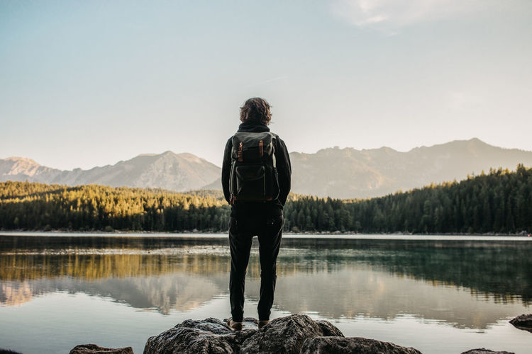 Rear view of man standing by lake against sky