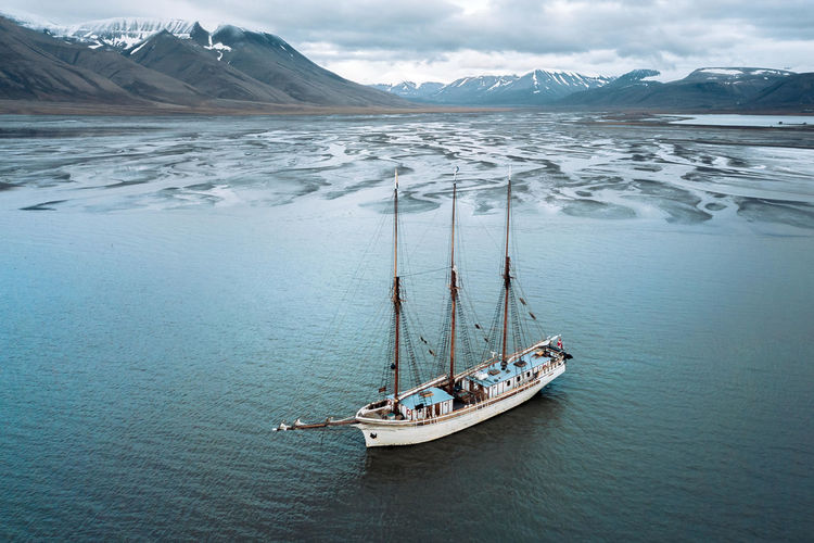 Boat moored in sea against mountains during winter