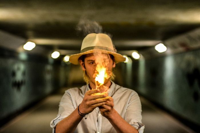 Portrait of mid adult man wearing hat holding fire while standing in tunnel