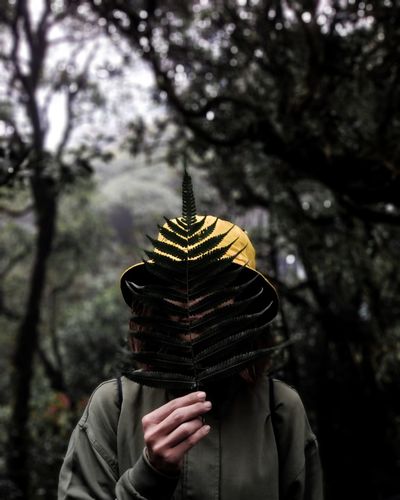 Woman holding fern leaves in front of face in forest