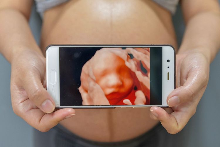 Midsection of pregnant woman holding mobile phone with baby ultrasound