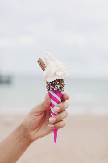 Hand holding ice cream cone against sea