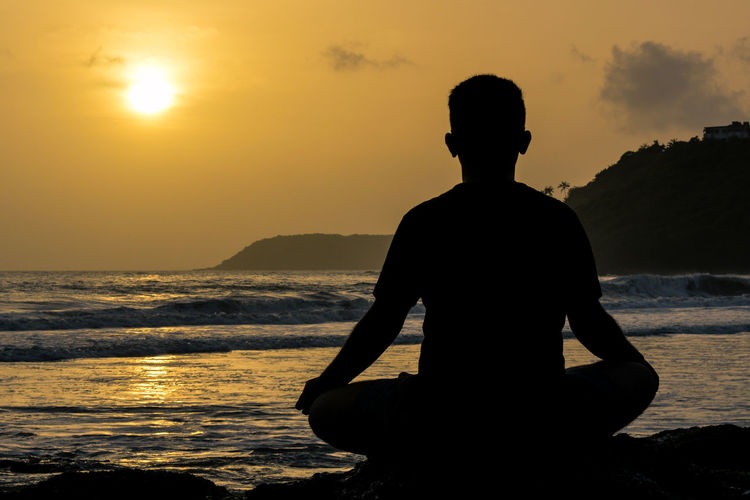 Silhouette man sitting on beach against sky during sunset