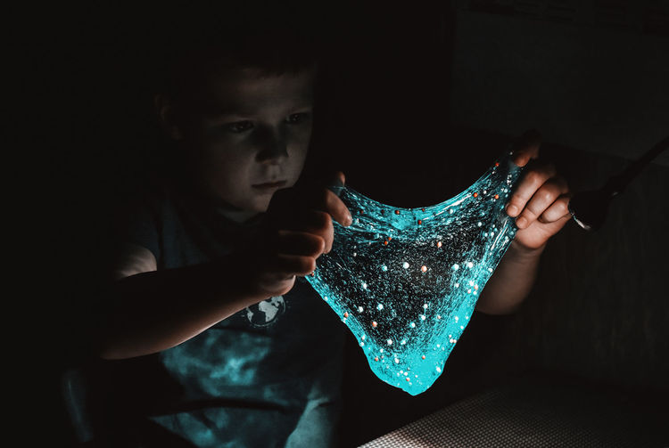 Portrait of boy holding slime in dark room