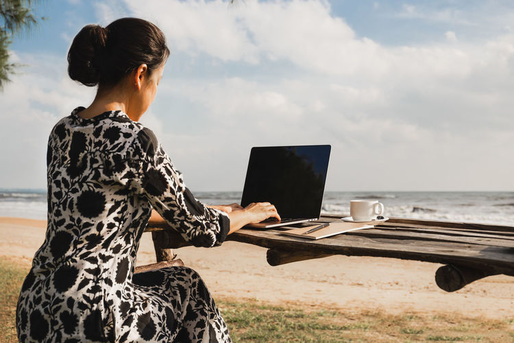 Business woman working on laptop computer on a beach on vacation.