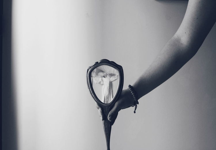 Close-up of hand holding mirror against wall