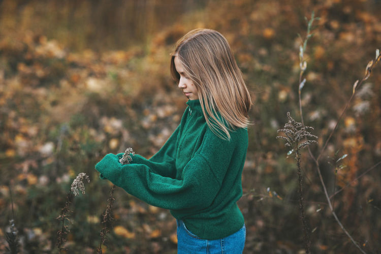 Portrait of a beautiful teenage girl with blond hair and blue eyes in an autumn park.