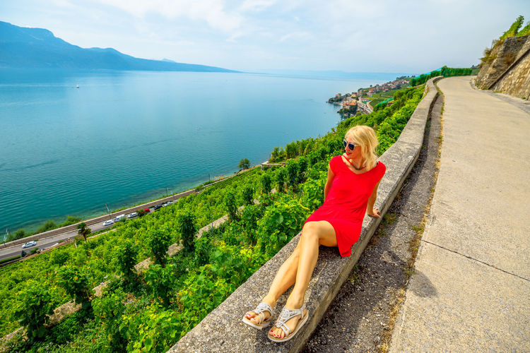 Full length of woman sitting by road against lake