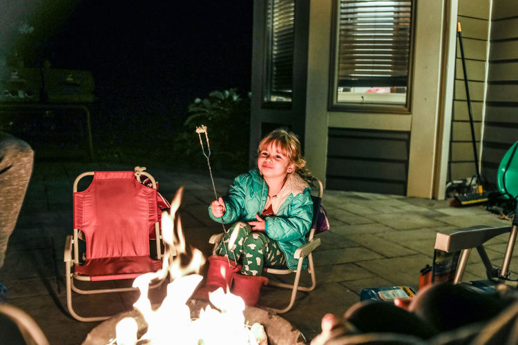 Little girl smiling while sitting in front of fire pit eating
