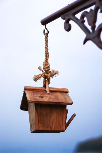 Low angle view of birdhouse hanging from hook against sky