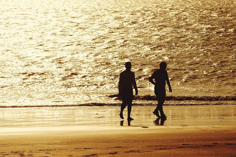 Silhouette of men walking at beach during sunset