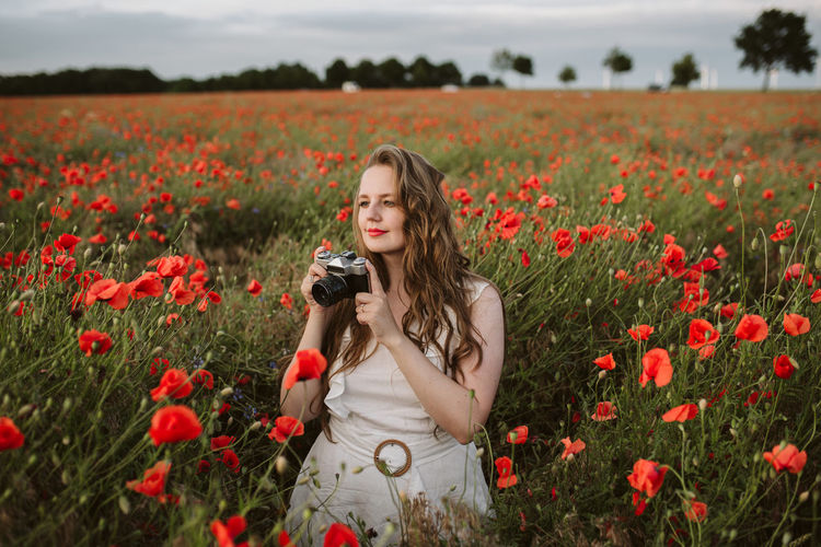 Portrait of young woman with red poppy flowers on field