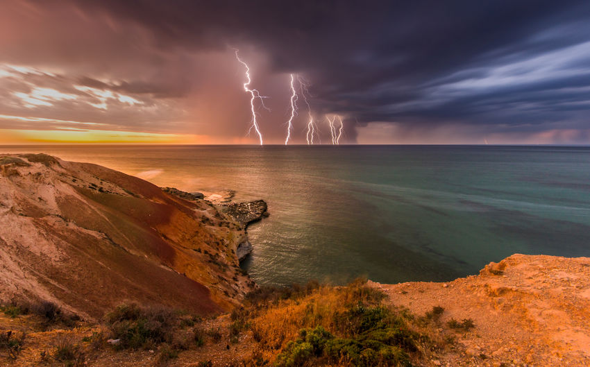 Scenic view of lightning over sea during sunset