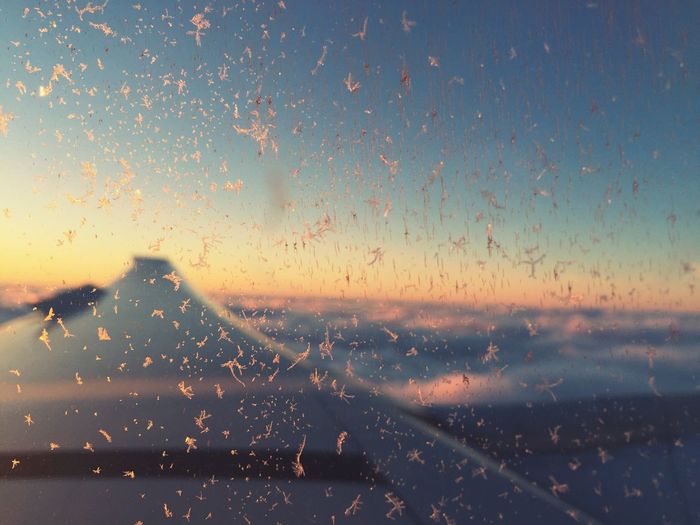 Close-up of snowflakes on airplane window against sky during flight