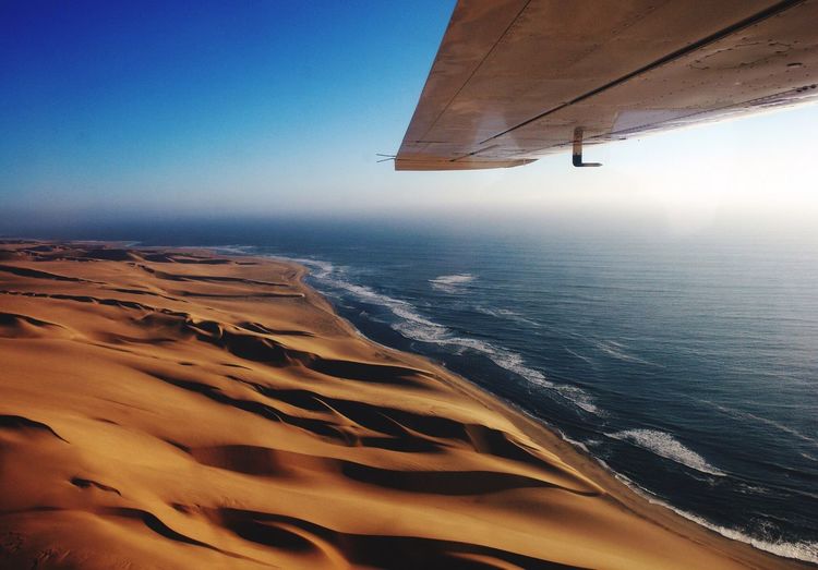 Aerial view of aircraft wing over sandy beach against blue sky