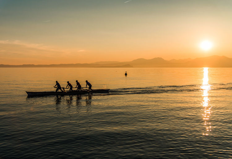 Silhouette men rowing boat on sea against sky during sunset