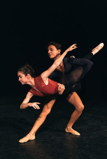 Full body danseur lifting ballerina while dancing on dark stage during rehearsal before performance in theater