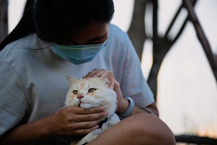 Young woman wearing mask petting cat