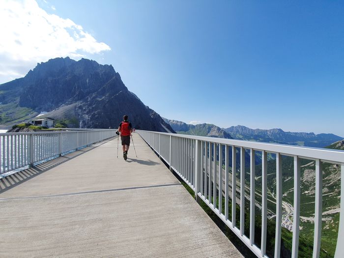 Rear view of man walking on footbridge against sky