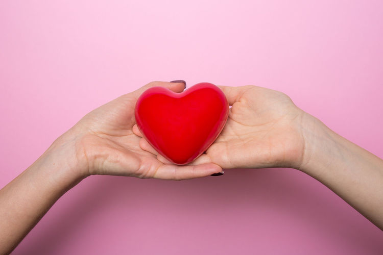 Close-up of woman hand holding heart shape over pink background