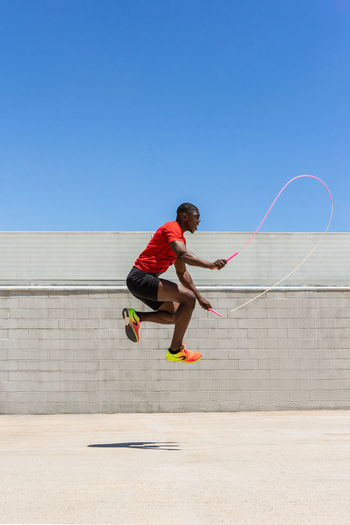 Side view of energetic african american male athlete skipping rope above ground while doing exercises during training in summer