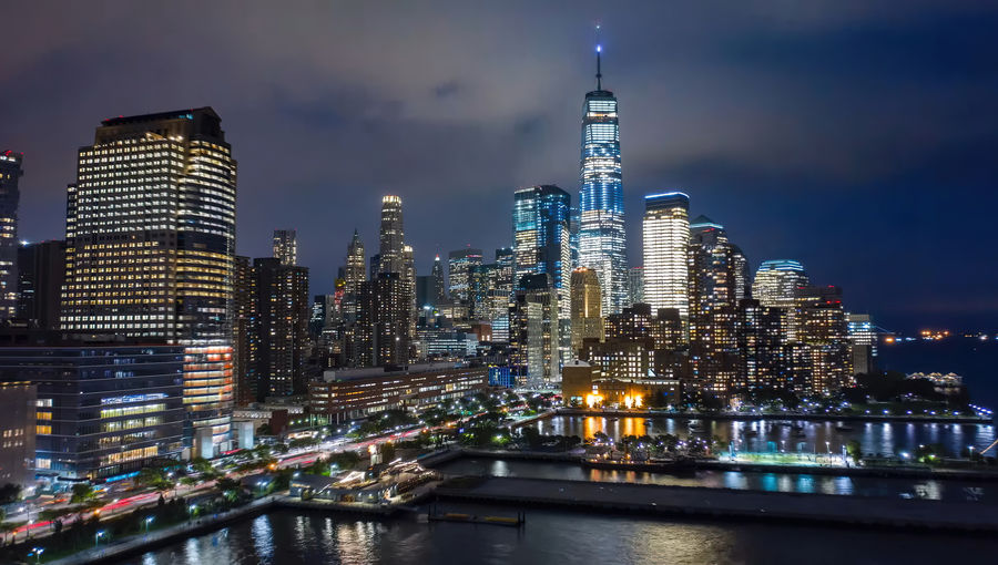 Illuminated buildings by river against sky at night