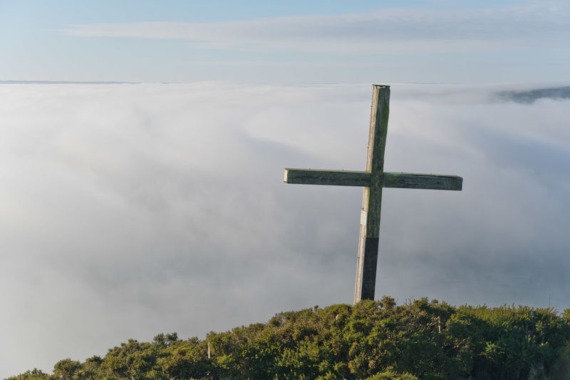 View of wooden cross on a hill looking down at a blanket of fog