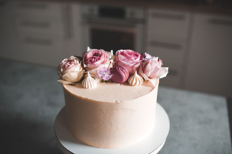 Tasty cake decorated with fresh flower roses staying on kitchen table closeup.