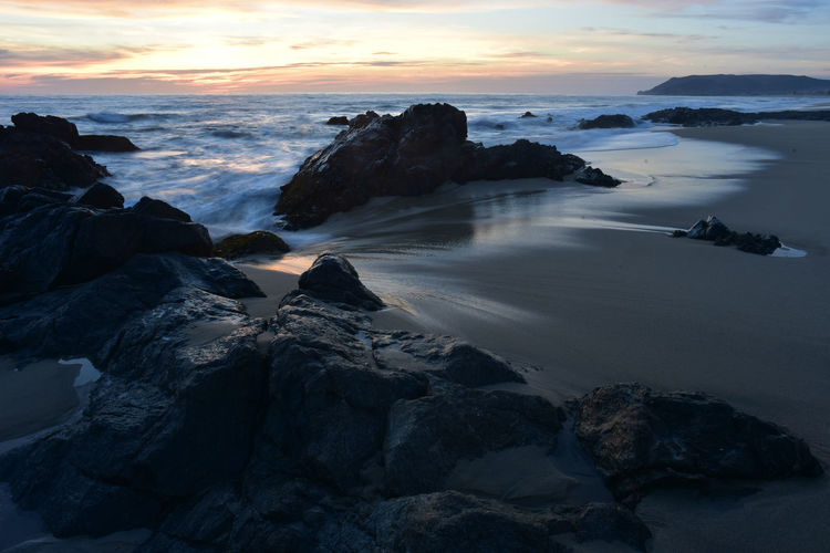 Rocks on beach against sky during sunset