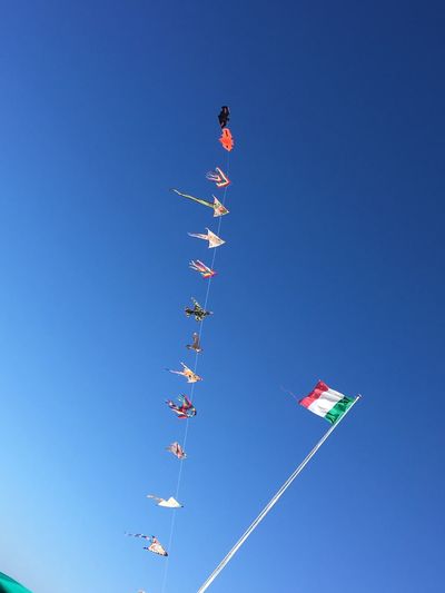Low angle view of kites and italian flag against clear blue sky