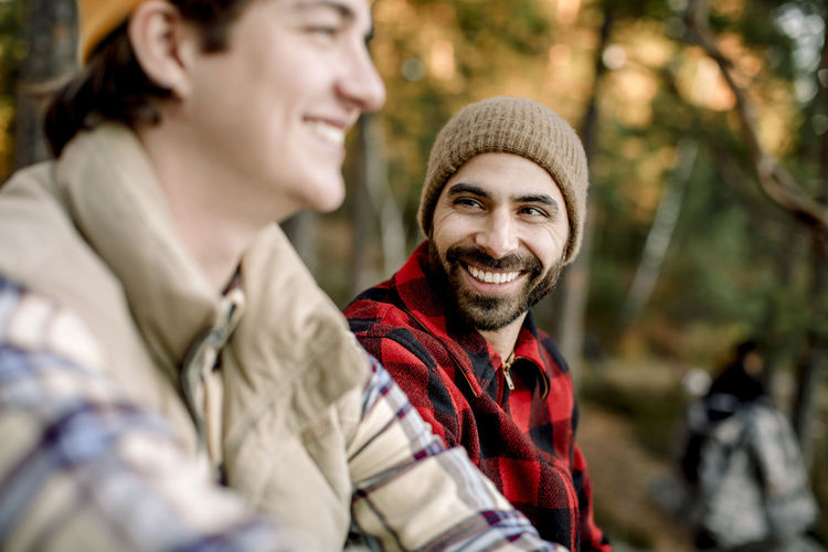 Happy man wearing plaid shirt talking to male friend during camping