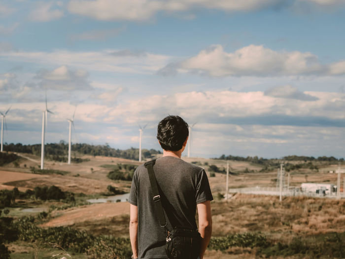 Rear view of man standing against windmills on landscape