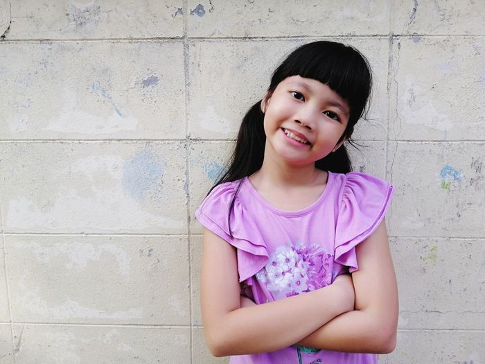Portrait of smiling girl standing with arms crossed against wall