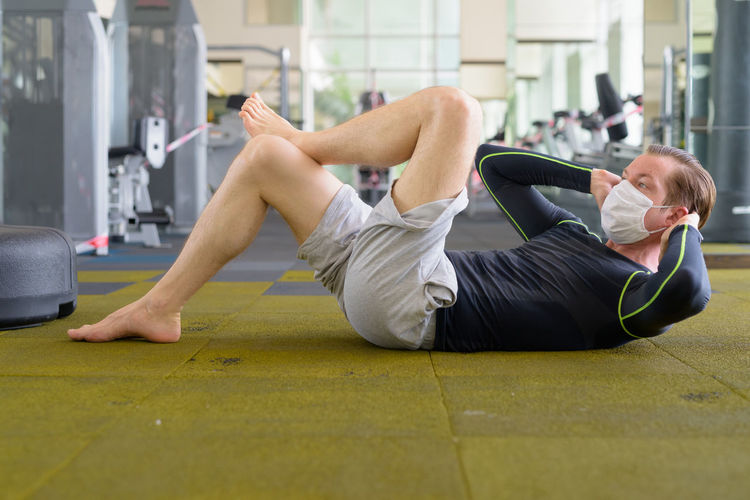 Full length of man exercising while lying down on floor at gym