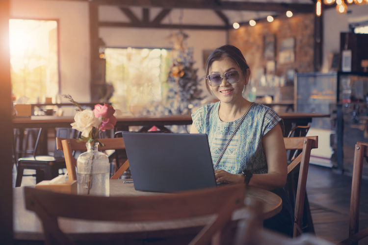 Portrait of smiling woman using laptop while sitting at cafe
