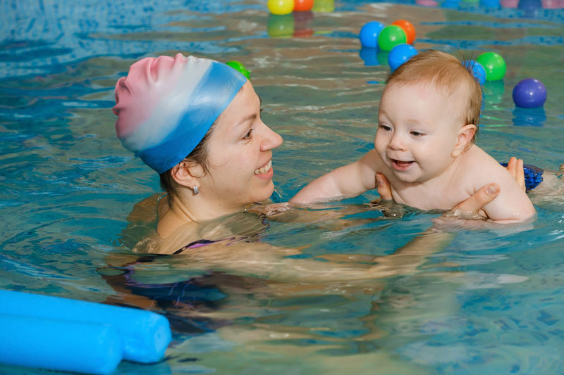 Early age swimming in pool. baby boy trained to swim in water coach woman in indoor swimming pool