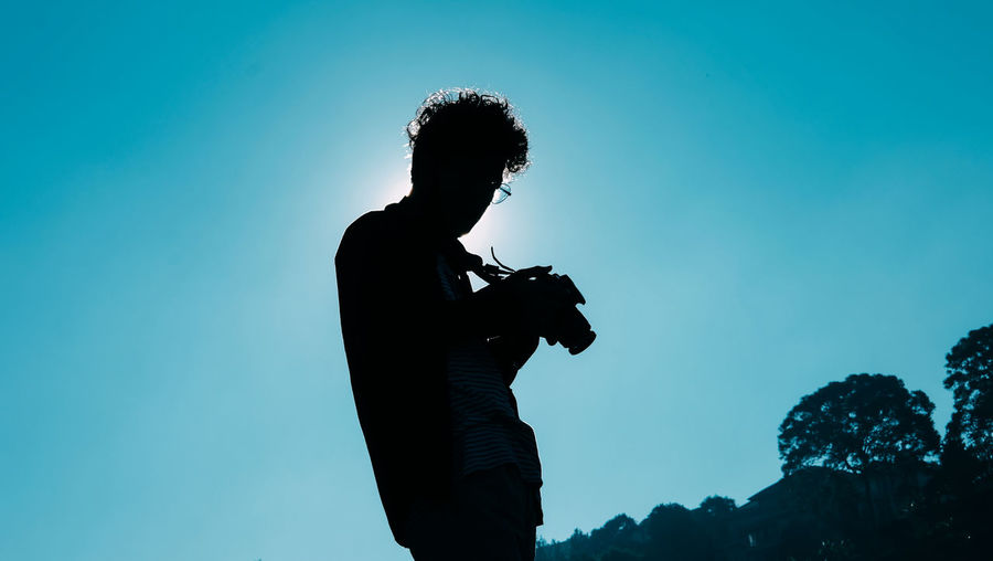 Low angle view of silhouette man standing against blue sky
